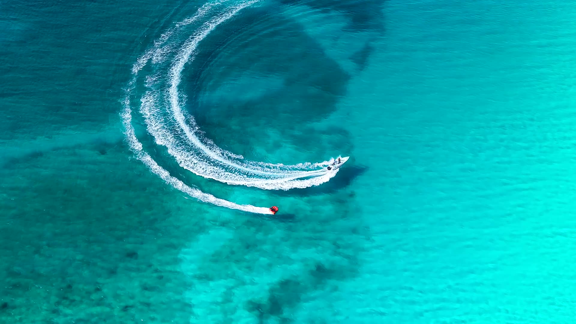 Vista aérea de una lancha que traza una curva blanca sobre agua turquesa